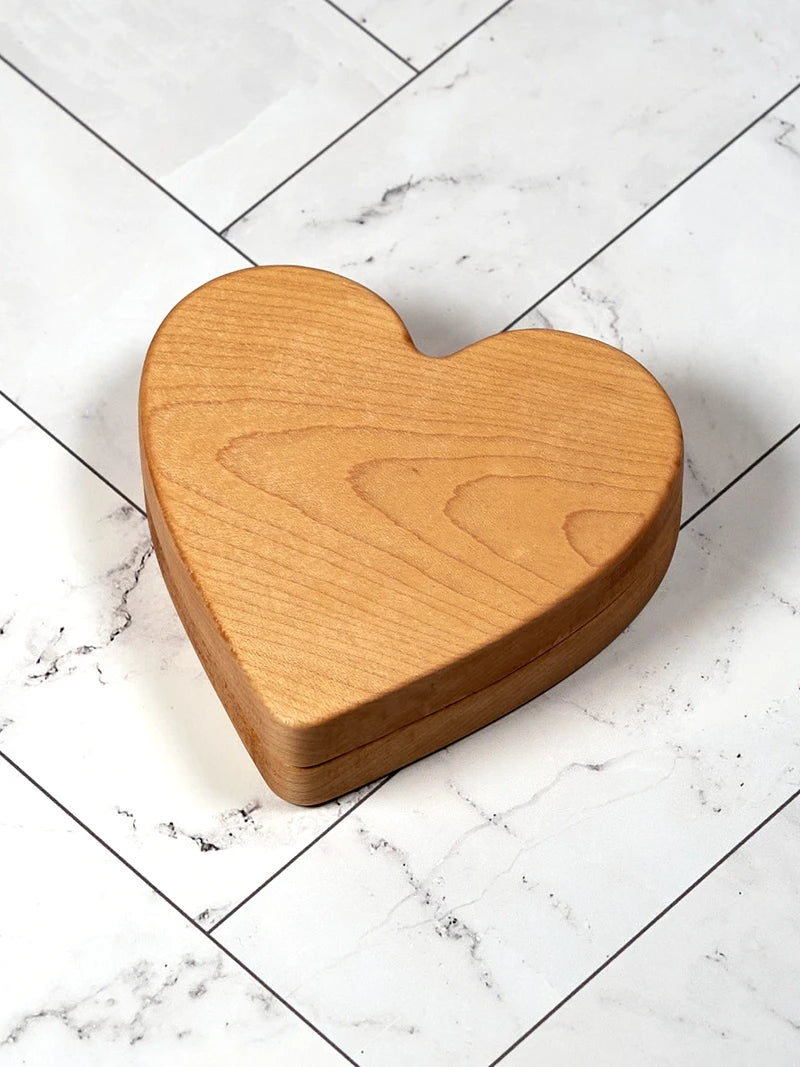Closed maple heart-shaped keepsake box on white marble tile, showing the grain of the lid.