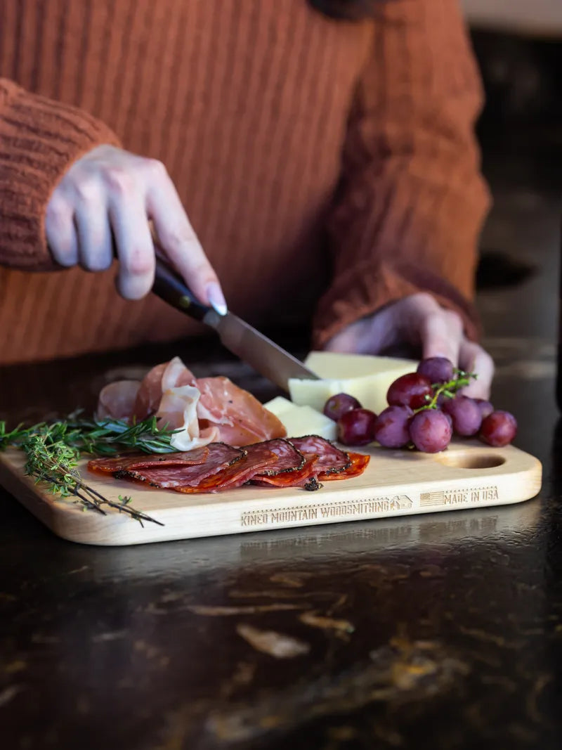 Hands prepping fresh ingredients on a small maple cutting board.