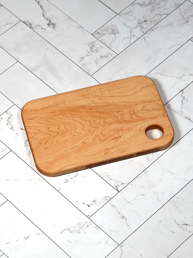 Handmade small hard maple cutting board on a white marble counter.