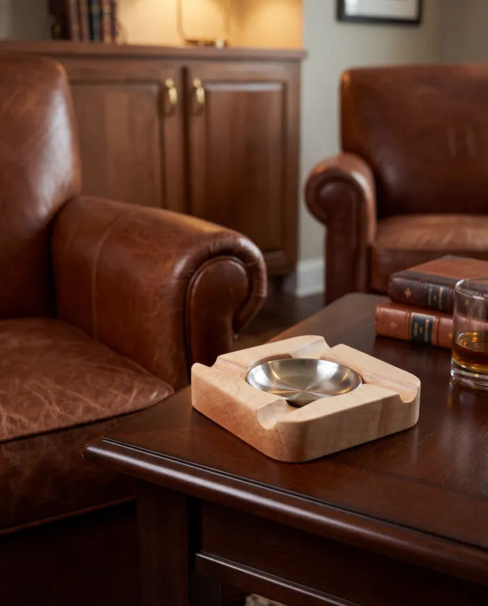 Maple cigar ashtray on a side table in a leather-chair lounge with a glass of whiskey.