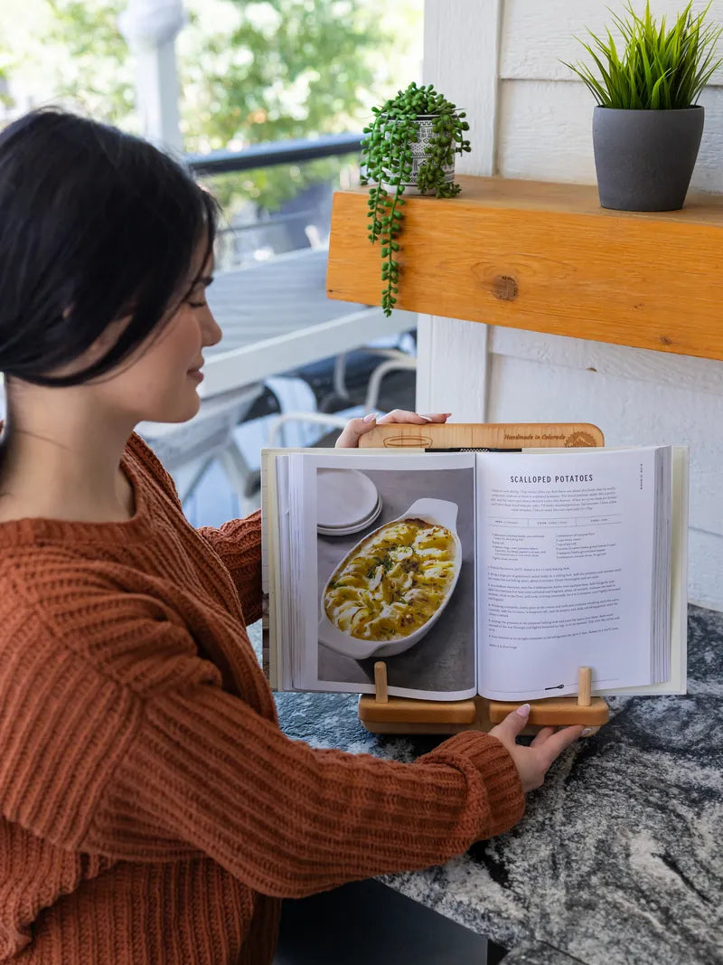 Woman reading from a cookbook propped in a wooden recipe book stand in a kitchen