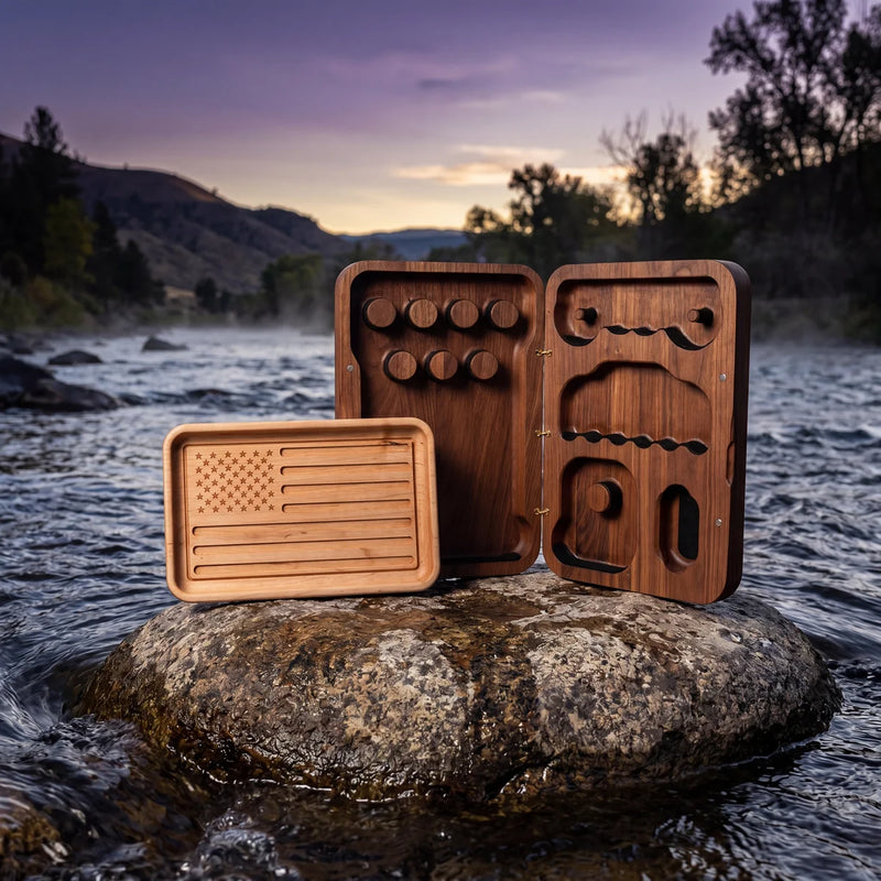 American flag engraved tray beside open walnut jewelry box with custom compartments on a river rock at dusk.