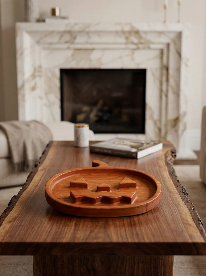 Premium cherry pumpkin tray with jack-o'-lantern design on wooden table in elegant living room setting with fireplace.