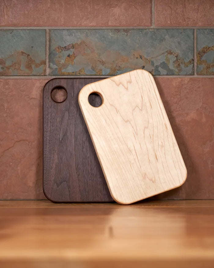 Small hard maple and walnut cutting boards stand upright, showing the grain and grip holes.
