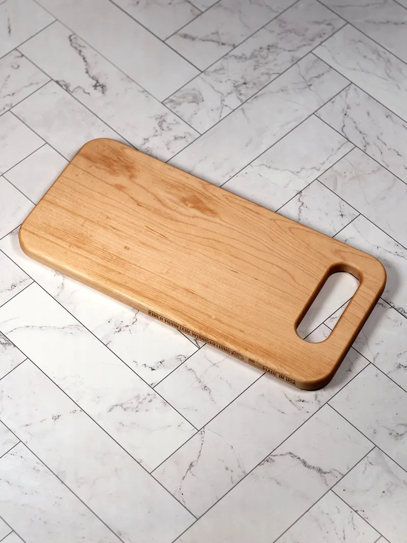 Hard maple bread board with handhold cutout, shown at an angle on white marble tile.