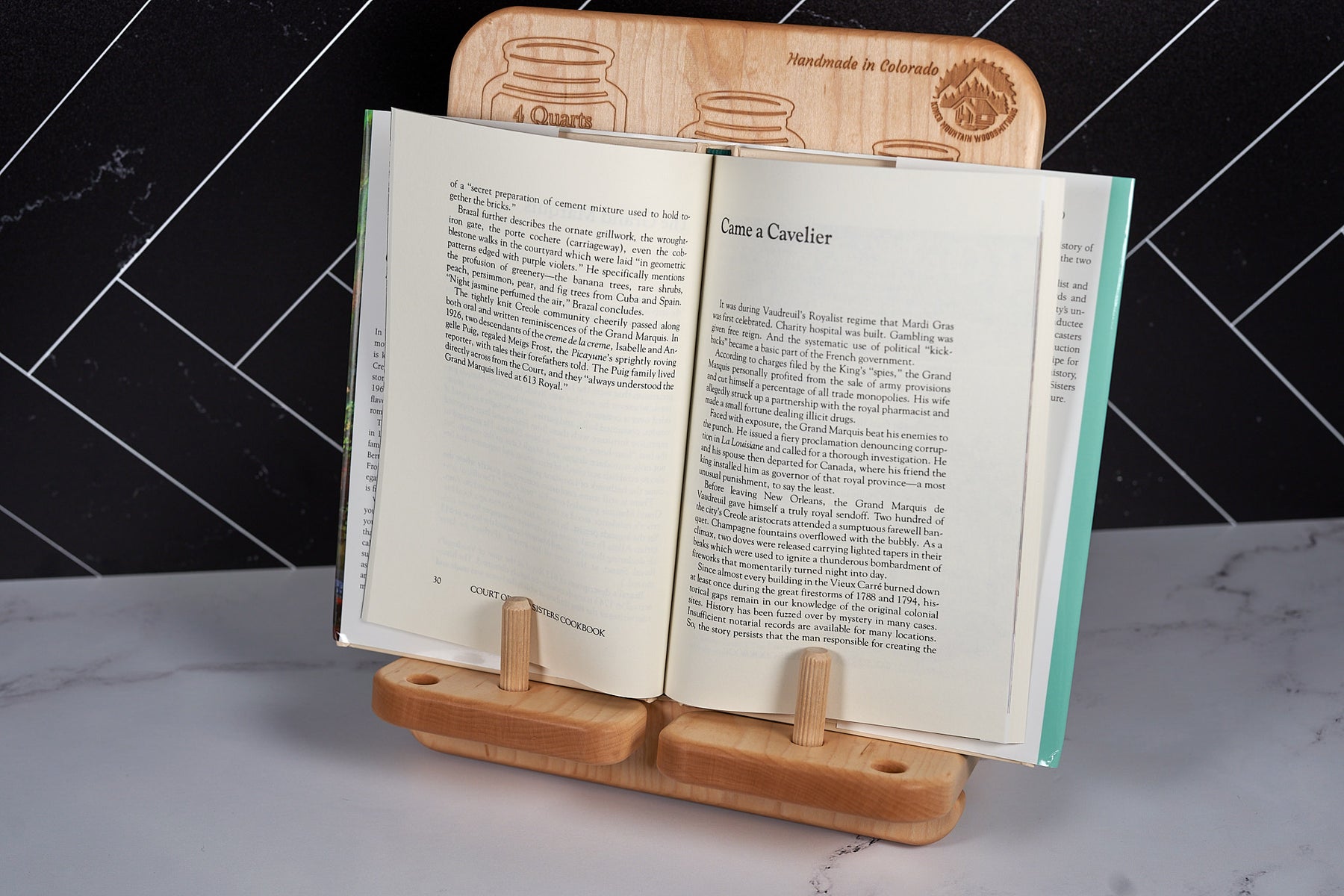 Premium maple cookbook holder with conversion chart propping open a cookbook on white marble kitchen countertop.