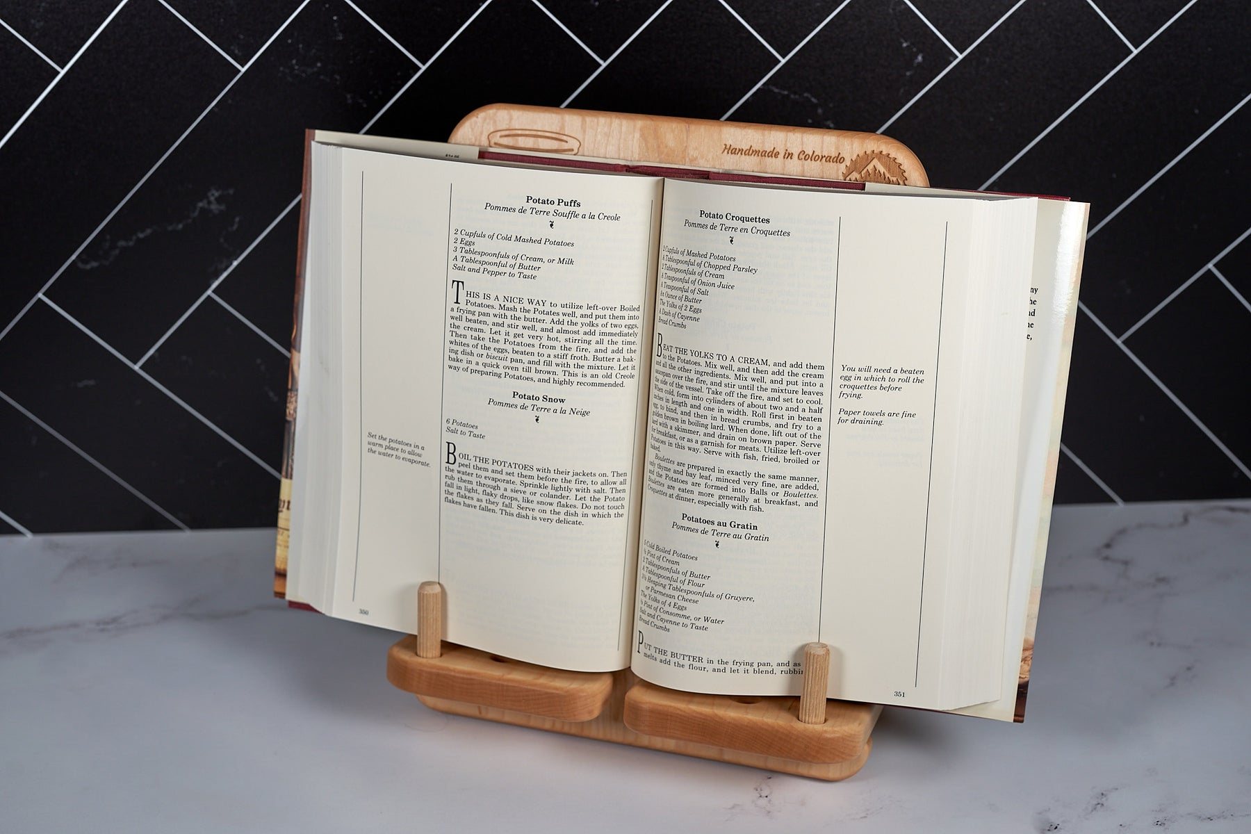 Elegant maple recipe stand with measurement conversions displaying an open book on marble counter in modern kitchen.
