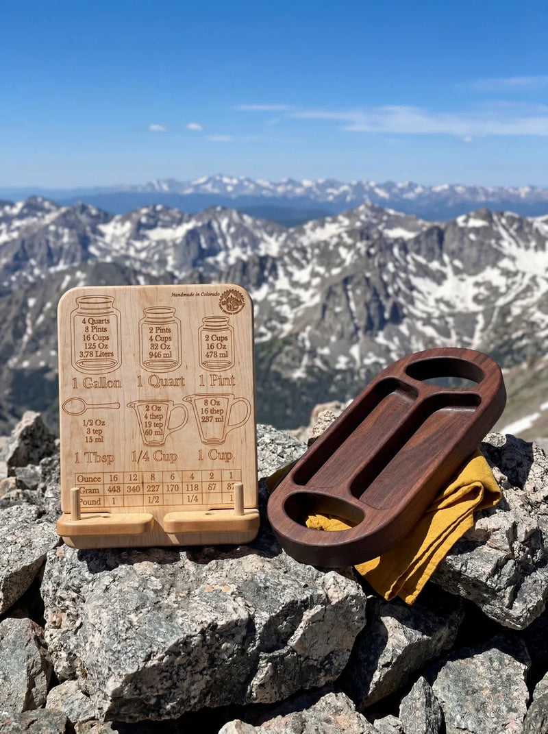 Elegant maple cookbook stand featuring measurement conversions next to walnut serving tray in mountain setting.
