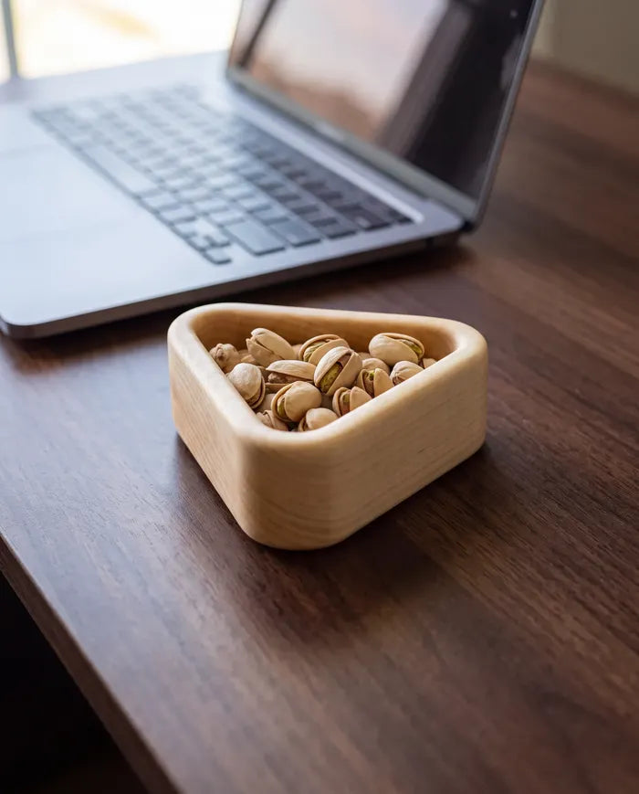 Small maple snack tray holding pistachios on a desk beside a laptop.