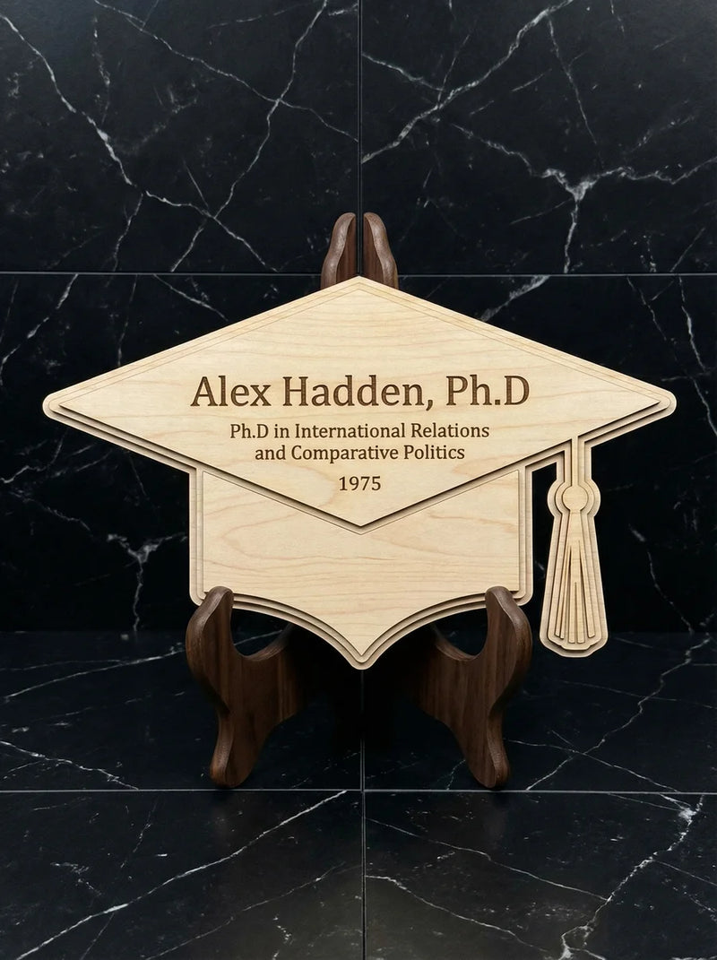 Personalized wood graduation cap plaque engraved with Ph.D name and details displayed on black marble surface.