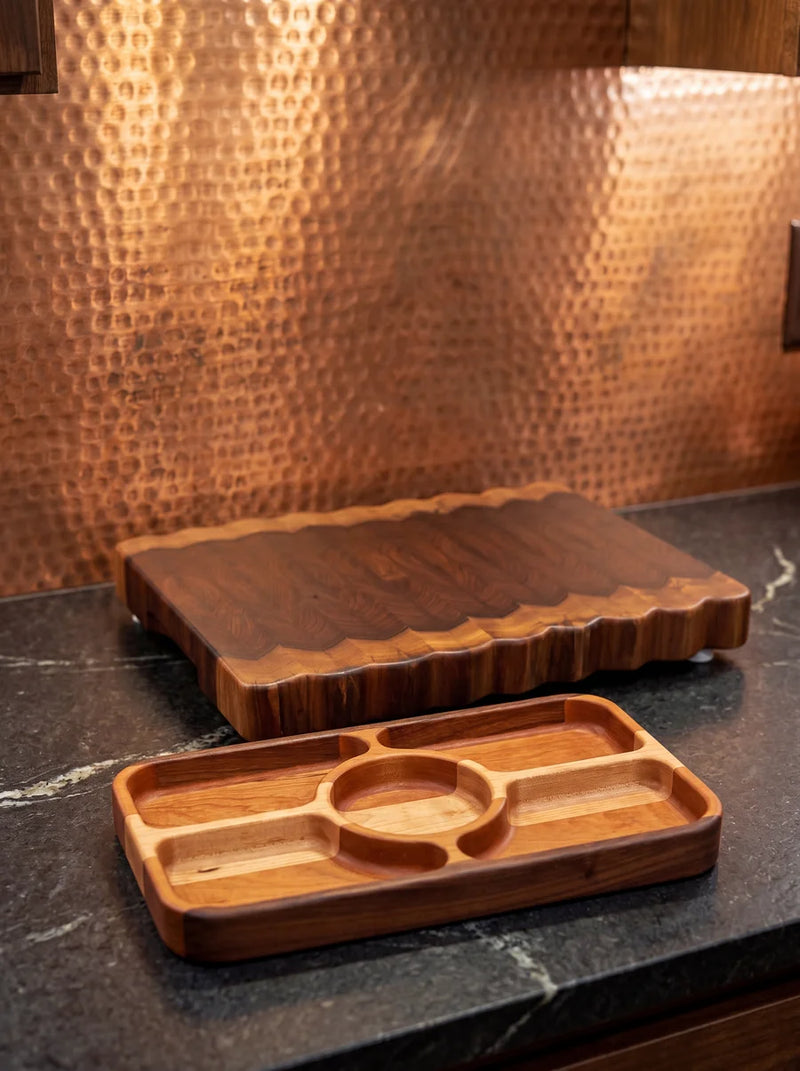 Rosewood live edge butcher block and cherry combo serving tray on marble counter with copper backsplash.