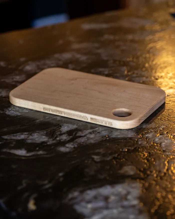 Handmade small maple cutting board resting on a dark slate countertop.