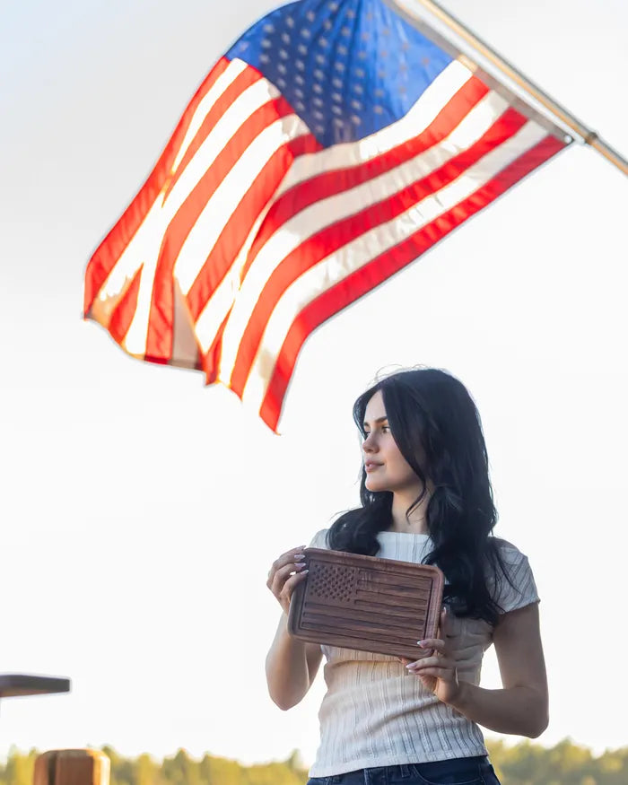 Walnut American flag catchall tray held outdoors with a flag flying behind.