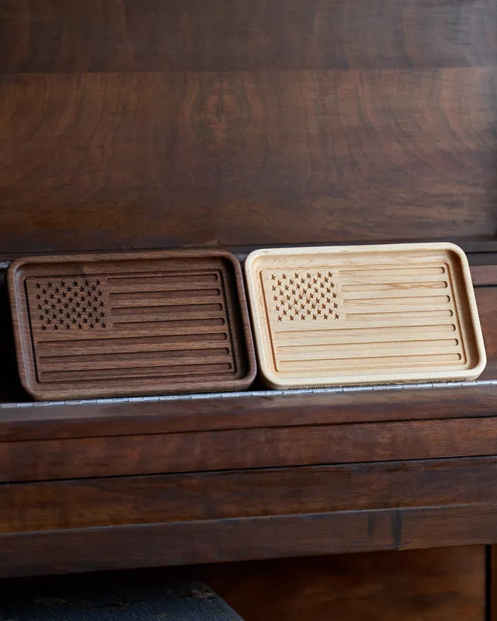 Walnut and hard maple American flag catchall trays side by side on a dark wood surface.