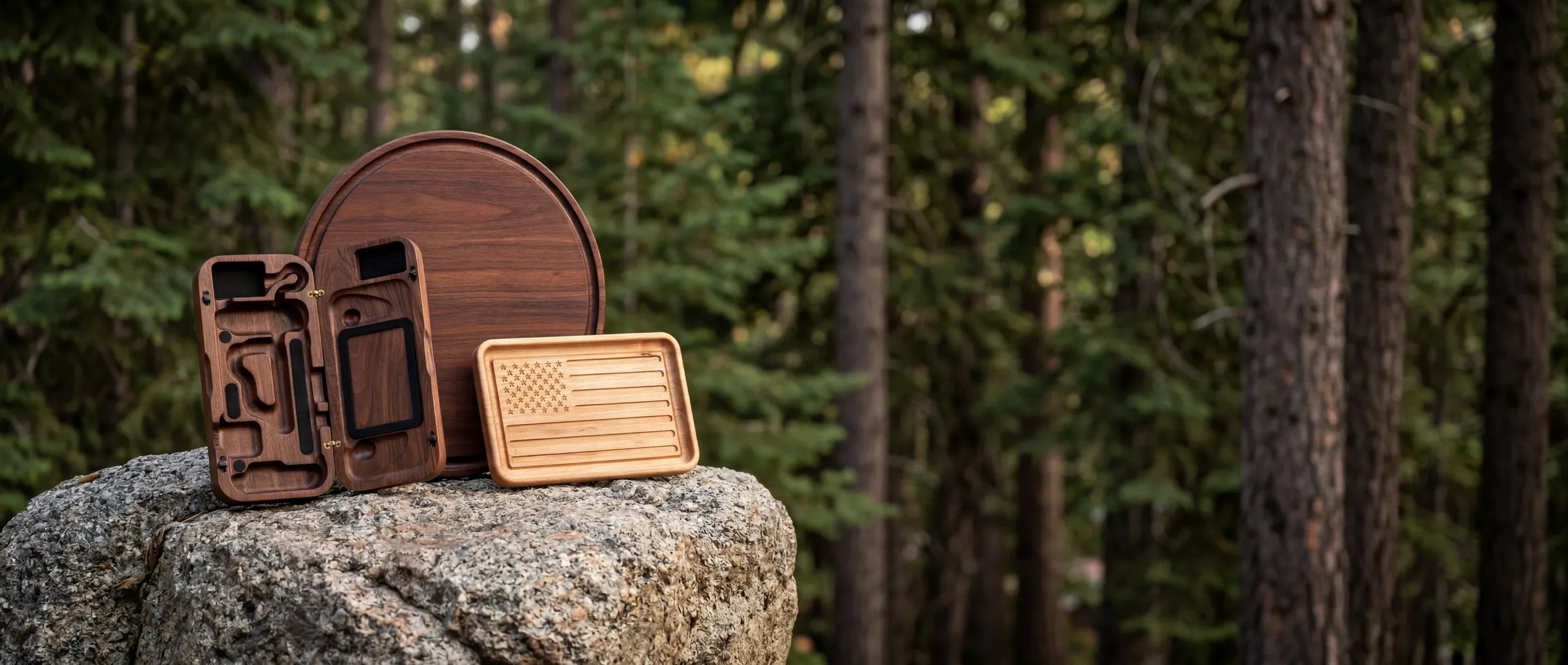 Elegant walnut Steam Deck case open with accessories compartments on rocky surface amid forest trees.