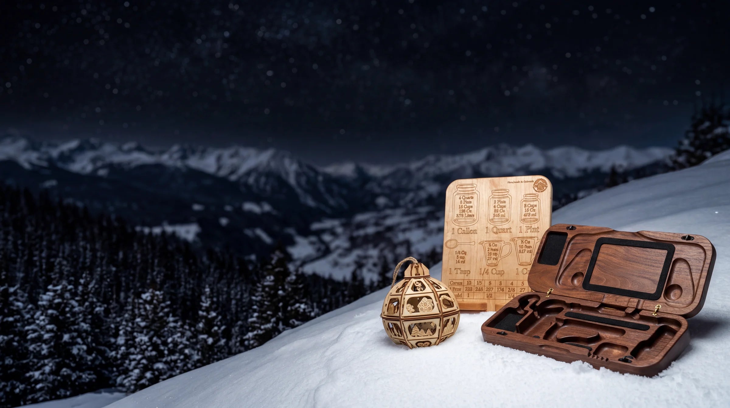 Walnut Steam Deck case open next to wood conversion chart cookbook stand and wood ornament on snow with starry mountain night view.